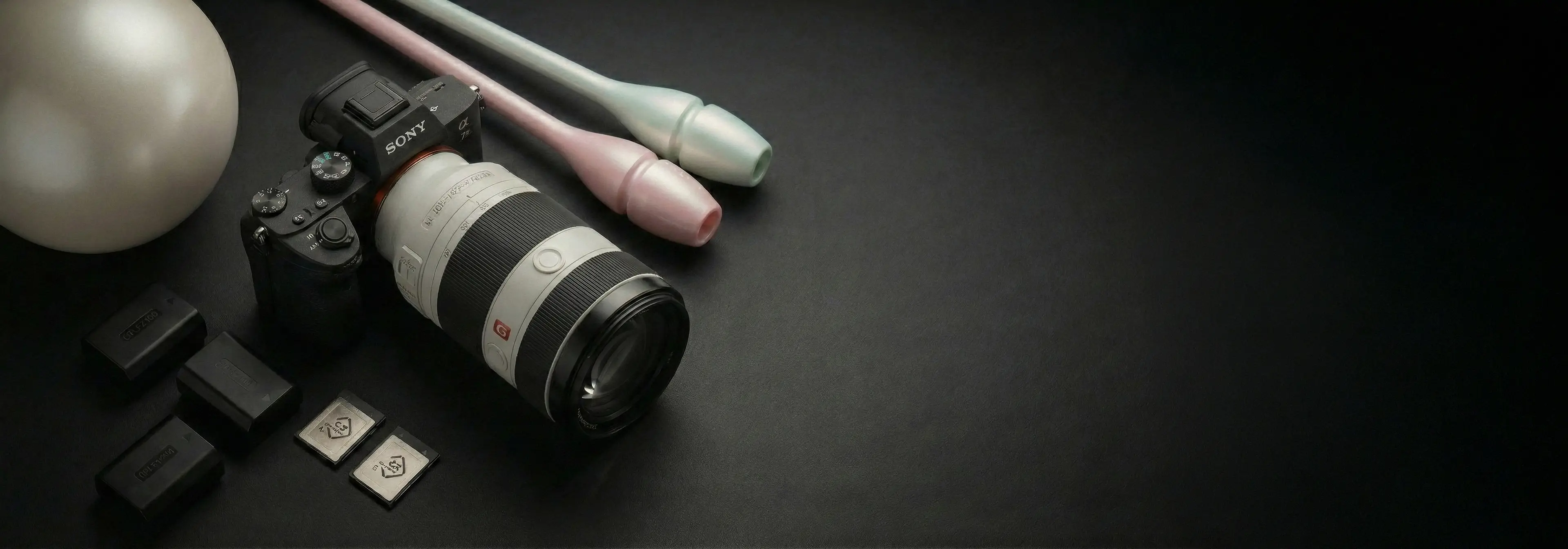 Sony camera with a telephoto lens next to rhythmic gymnastics clubs and ball